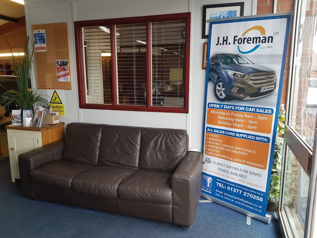 Sign for J.H. Foreman Ltd with car sales information next to a brown leather sofa in a shop interior.