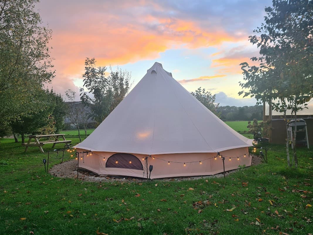Glamping tent with soft lighting, surrounded by greenery and trees, under a colorful sunset sky in Hutton-le-Hole.