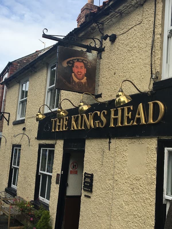 The Kings Head pub features a sign with a man's portrait and golden lettering, surrounded by outdoor lighting.