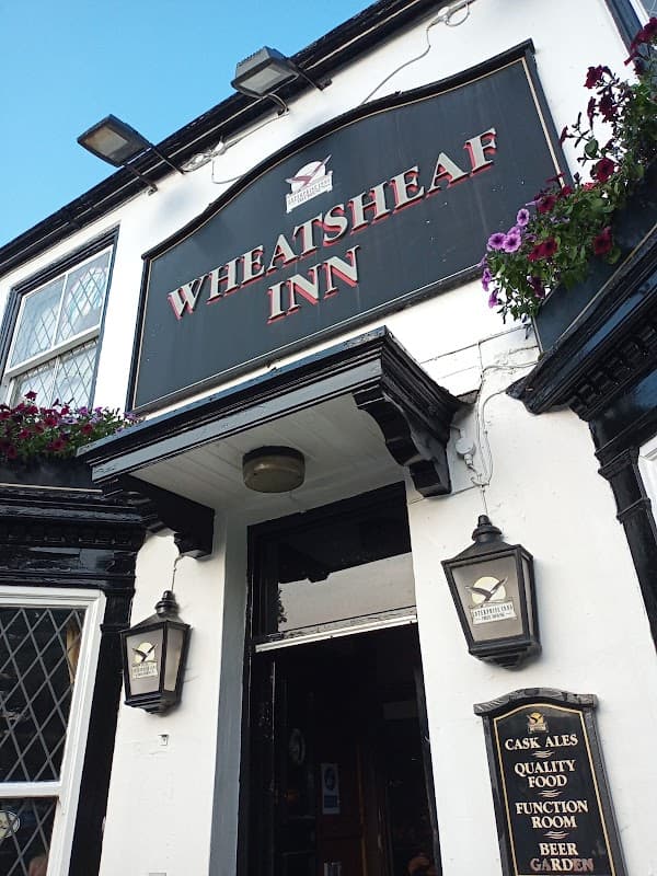 Signage of Wheatsheaf Inn with hanging flower baskets, lanterns, and a menu board outside the entrance.