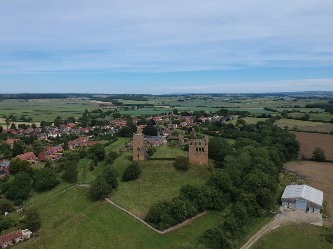 Aerial view of Sheriff Hutton Village Hall surrounded by green fields and historic ruins, with a village in the background.