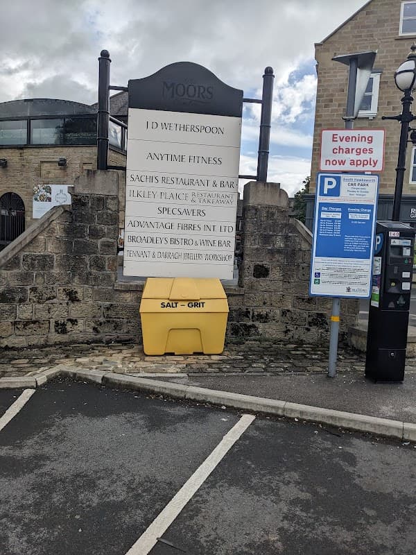 Signage for local businesses and parking information, with a yellow salt grit bin in the foreground.