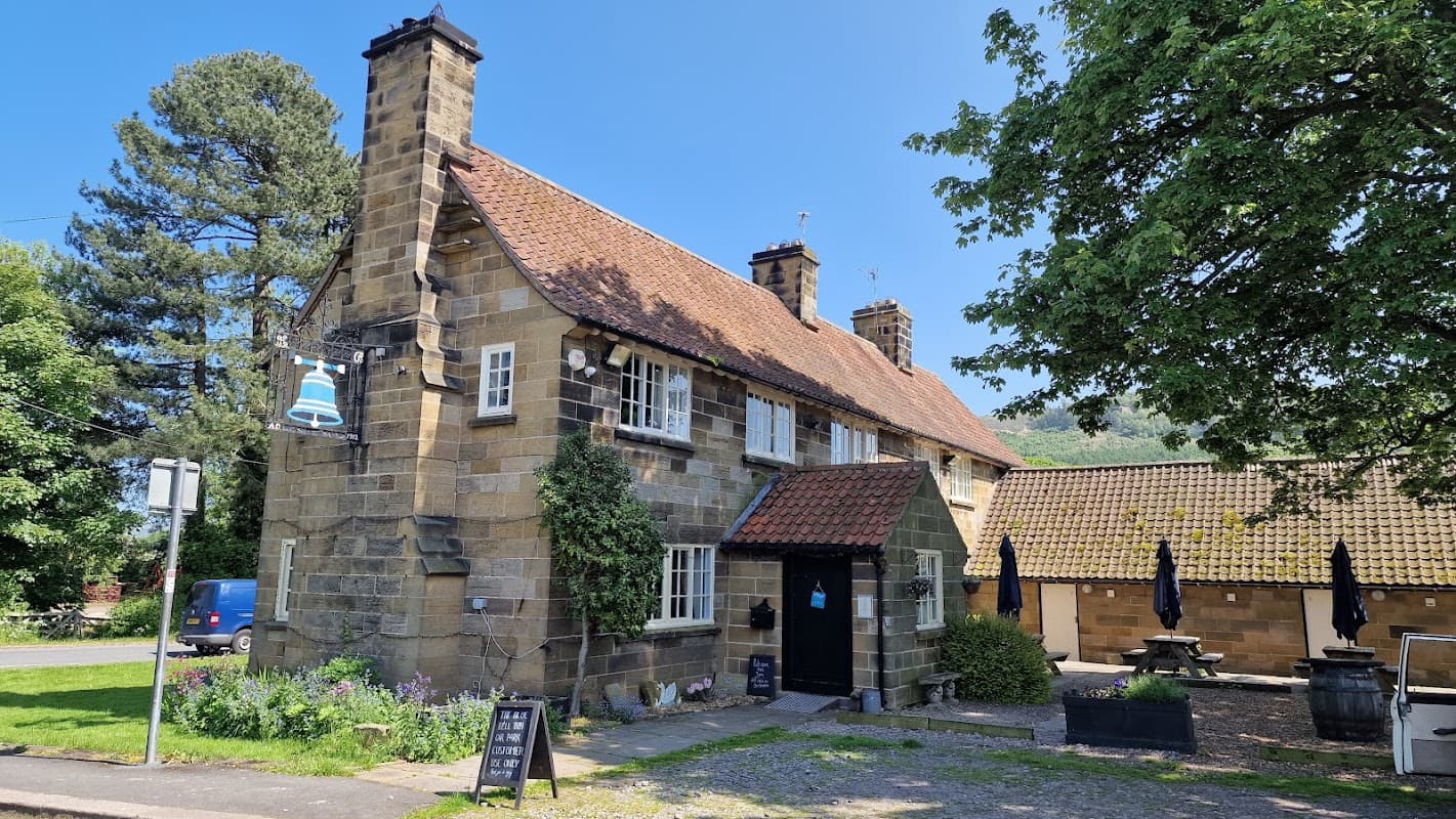 Charming stone building with a red-tiled roof, surrounded by greenery and outdoor seating, in a sunny Yorkshire setting.