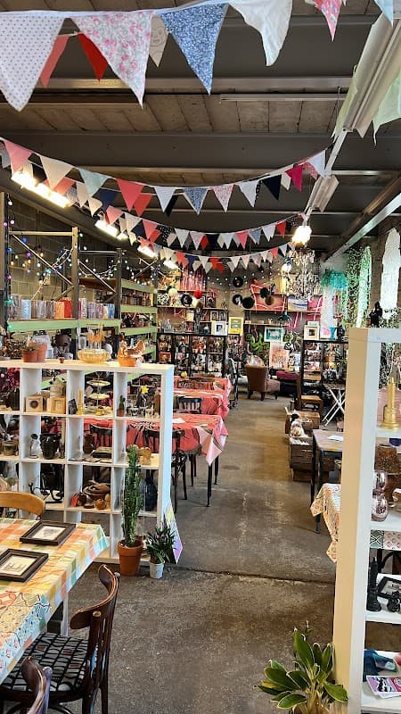 Colorful bunting decorates the ceiling of a cozy shop filled with vintage items and plants, creating a warm atmosphere.