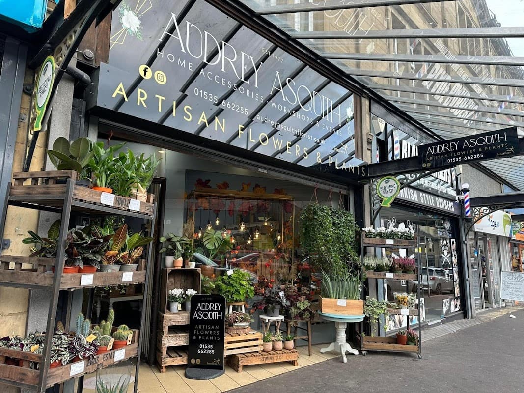 Floral shop entrance with diverse plants, flowers, and decorative items, featuring a sign for "Audrey Asquith".