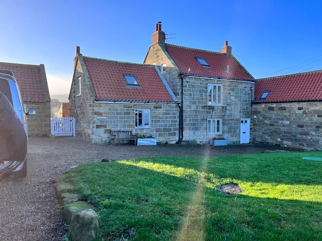 Stone building with red roof, grassy area, and clear blue sky in Kettleness, Yorkshire.