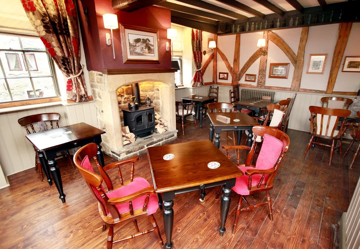 Cozy bar interior with wooden tables, chairs, a stone fireplace, and framed pictures on the walls.