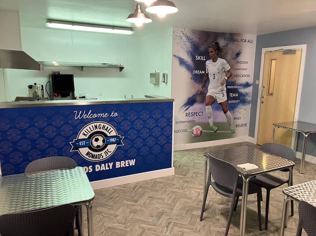 Bright café interior with metal tables, a welcoming sign, and a mural of a female soccer player on the wall.