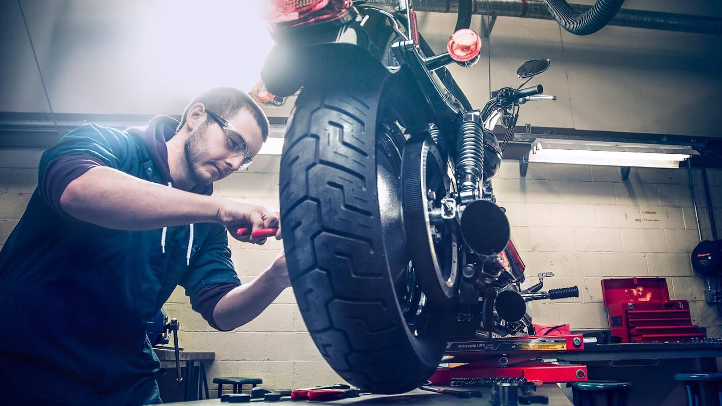 A mechanic working on a motorcycle in a garage, with tools and equipment visible in the background.