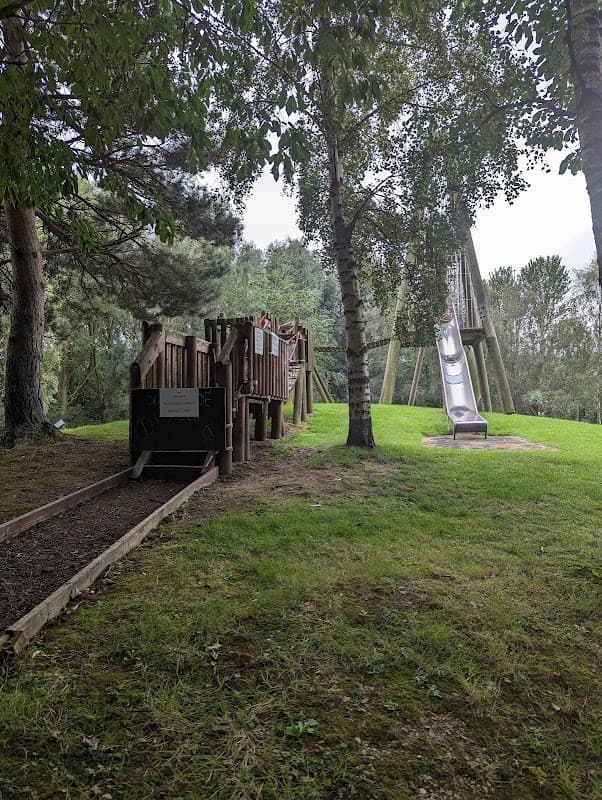 Wooden playground structure with slide, surrounded by trees and grassy area at Playworld, Kinsley, Yorkshire.