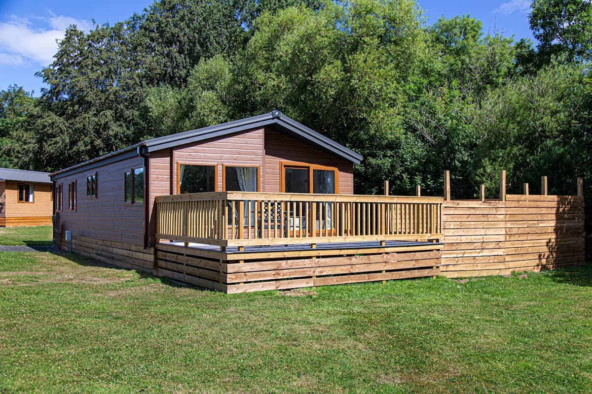 Wooden lodge with a deck, surrounded by greenery and trees, set in a grassy area at Kiplin Lodge Park.