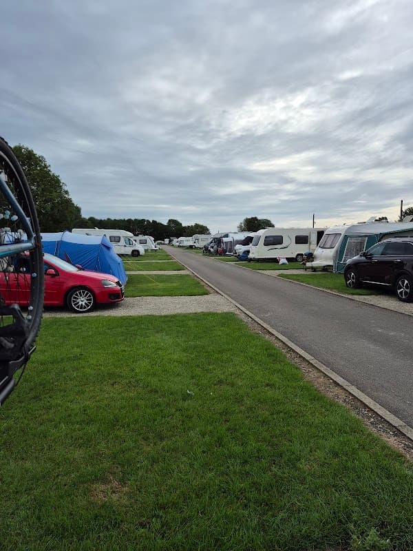 Campsite with caravans and tents lined along a grassy path under a cloudy sky in Kirby Misperton, Yorkshire.