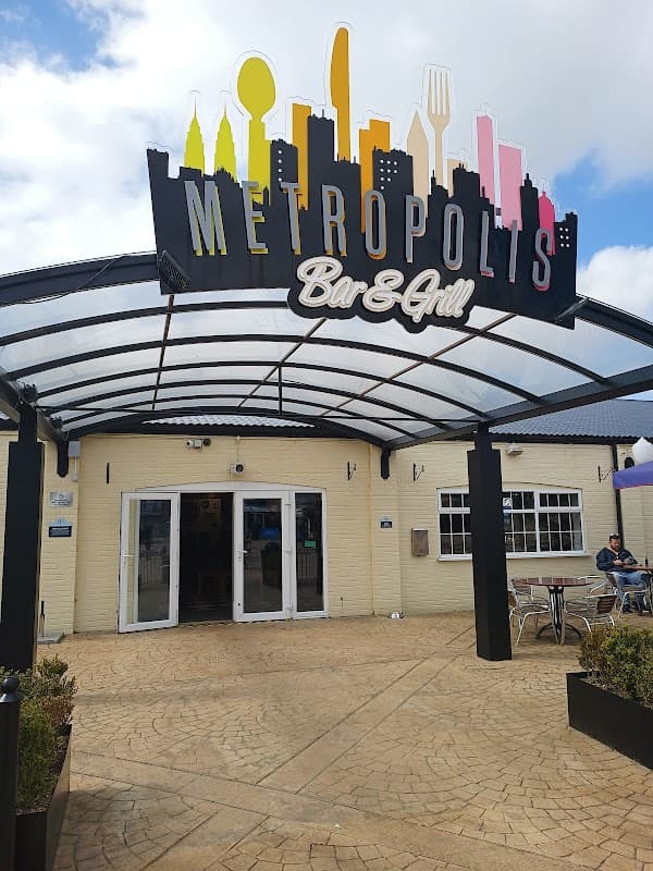 Entrance to Metropolis Bar & Grill featuring a colorful skyline sign and outdoor seating area in Kirby Misperton.