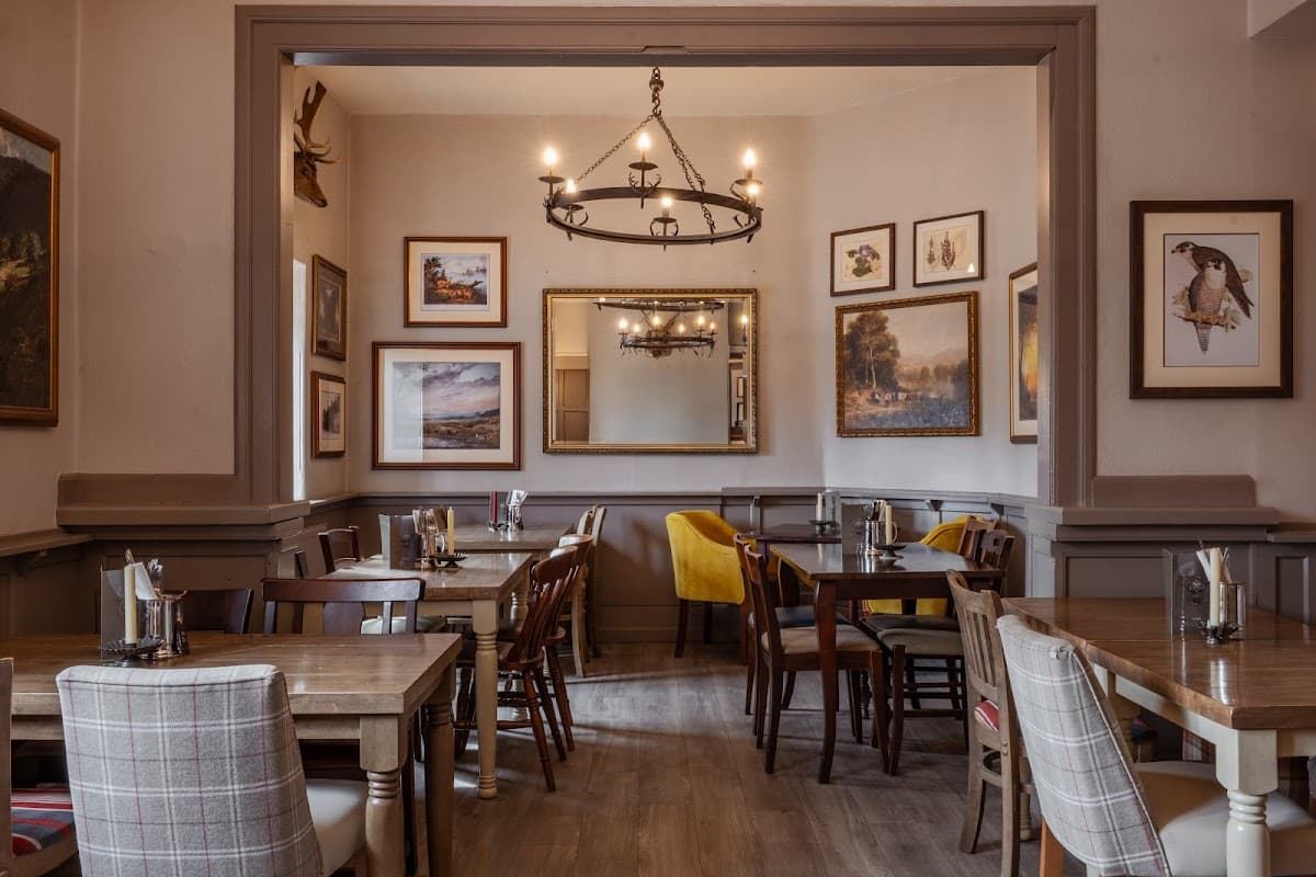 Cozy restaurant interior with wooden tables, chairs, framed artwork, and a chandelier in a welcoming atmosphere.