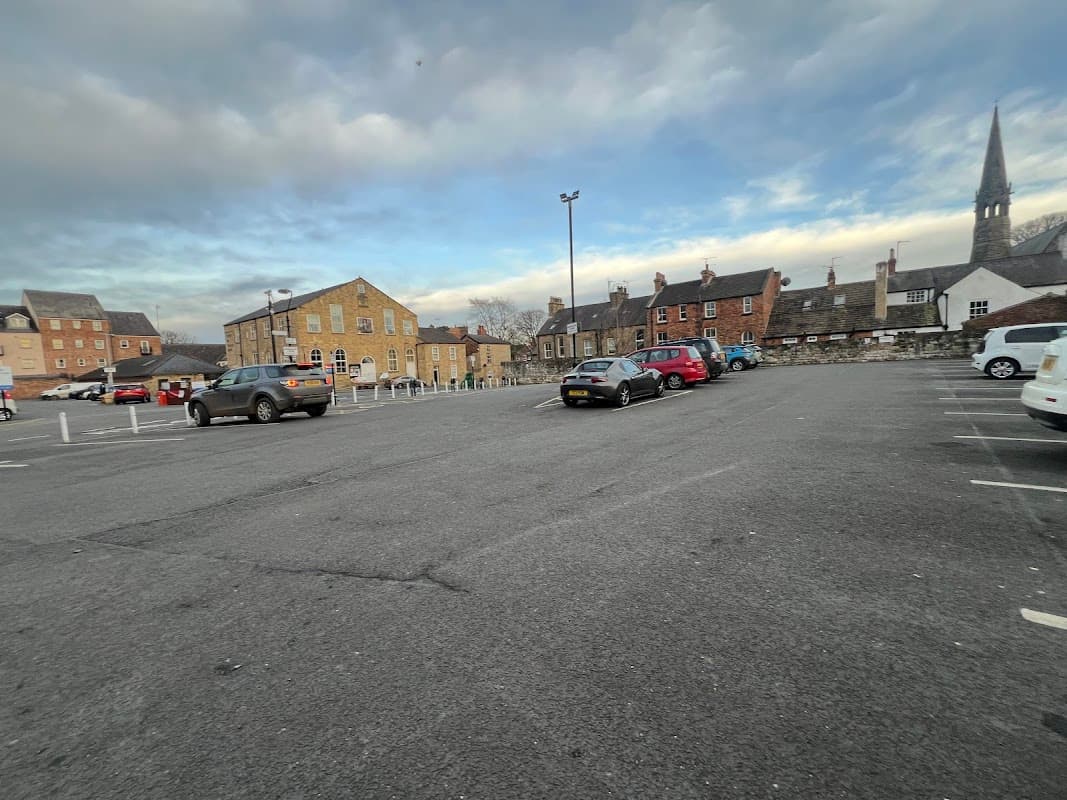 Chapel Street car park in Knaresborough, featuring several parked cars and historic buildings under a cloudy sky.