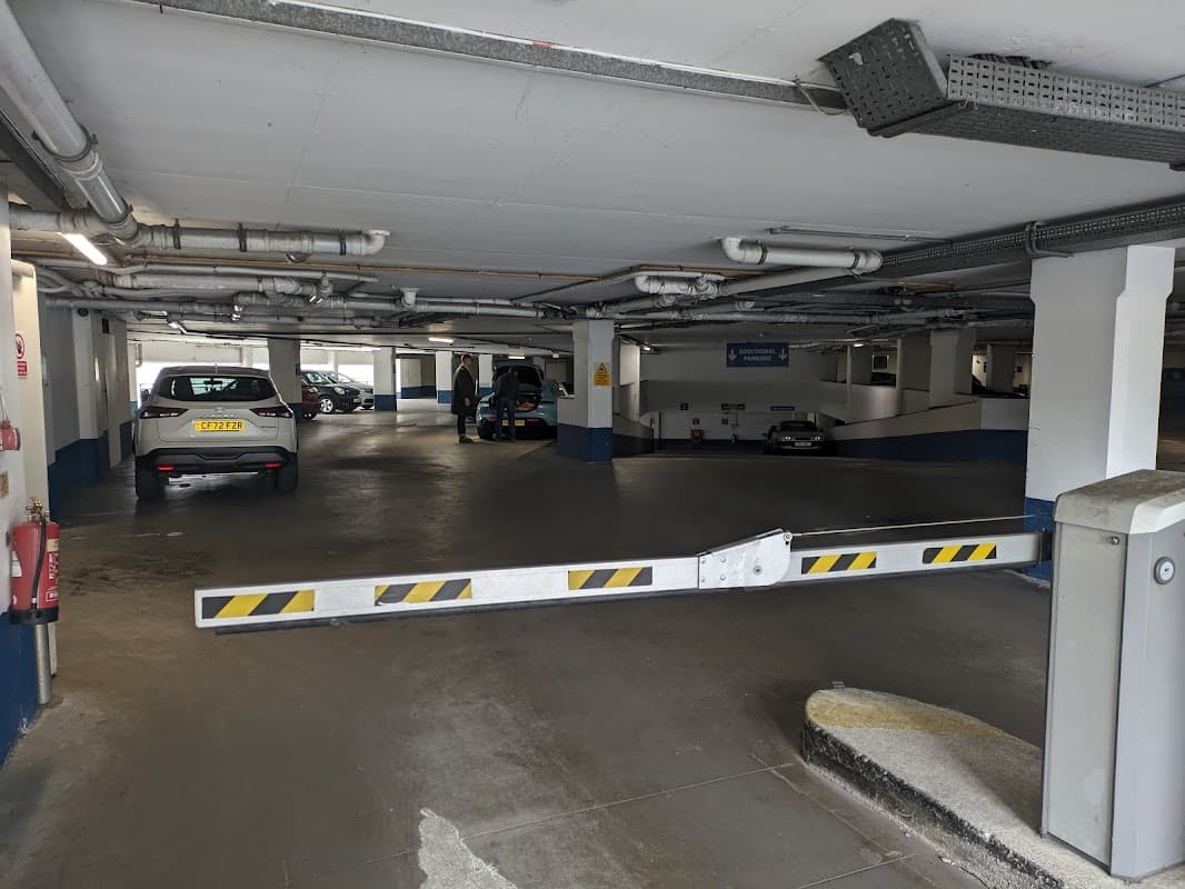 Pay & Display car park with parked cars, a barrier, and visible signage in a multi-level structure.