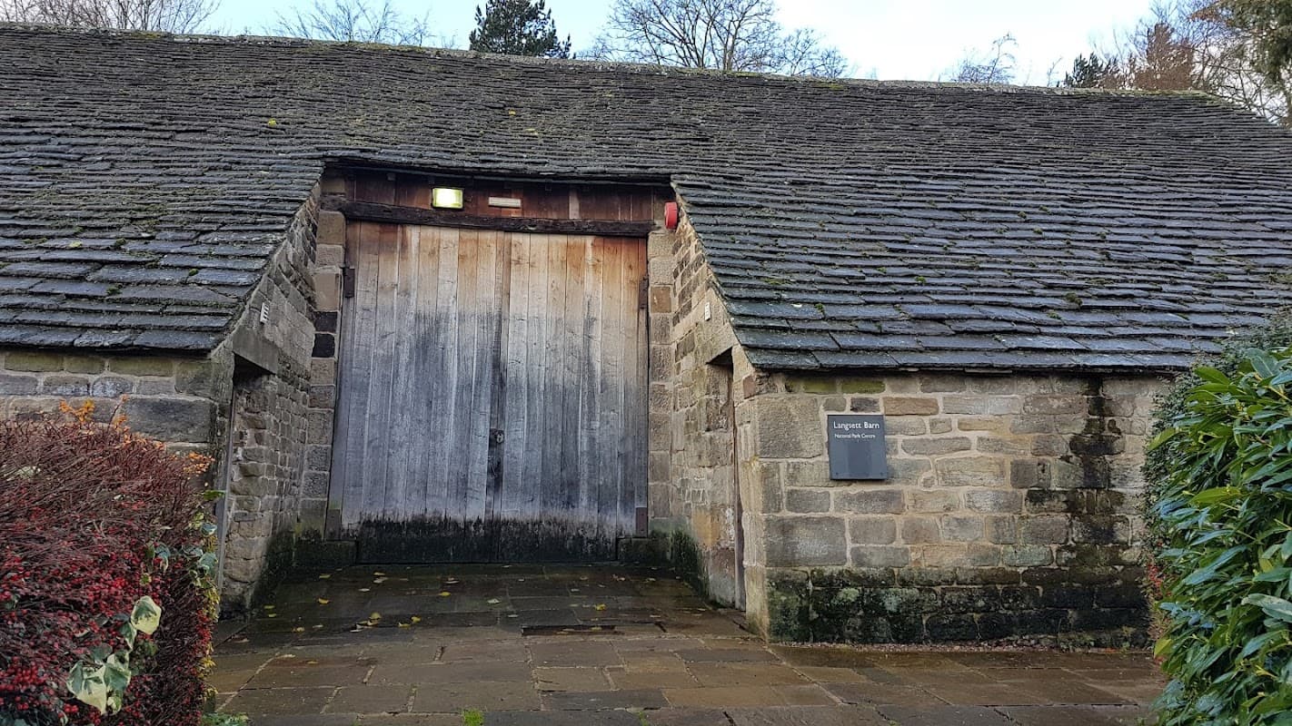 Weathered stone barn with a wooden door, surrounded by greenery and trees in Langsett, Yorkshire.