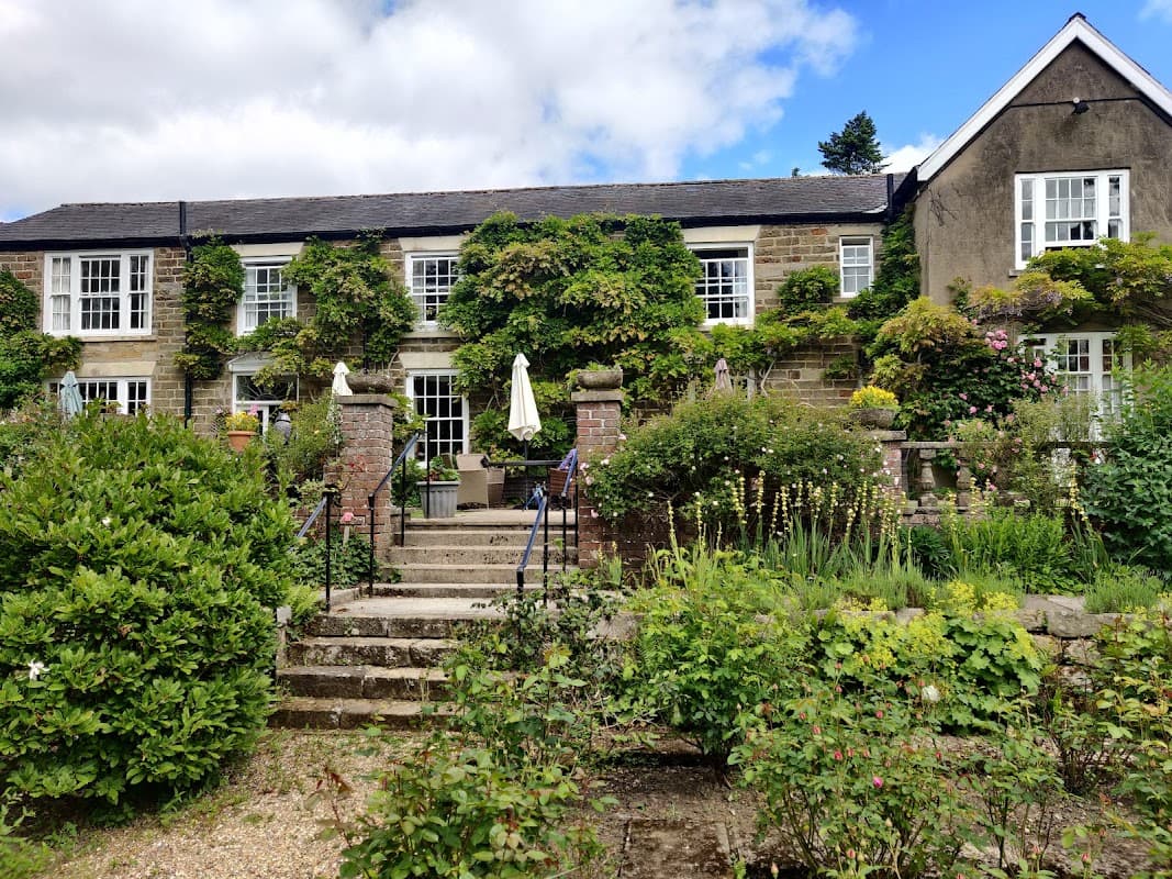 Charming country house hotel with lush greenery, stone steps, and outdoor seating under umbrellas in Lastingham, Yorkshire.