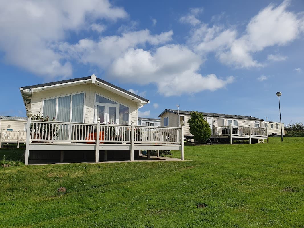 Two holiday cabins with wooden decks on a grassy area, under a blue sky with fluffy clouds at Haven Blue Dolphin Touring Site.
