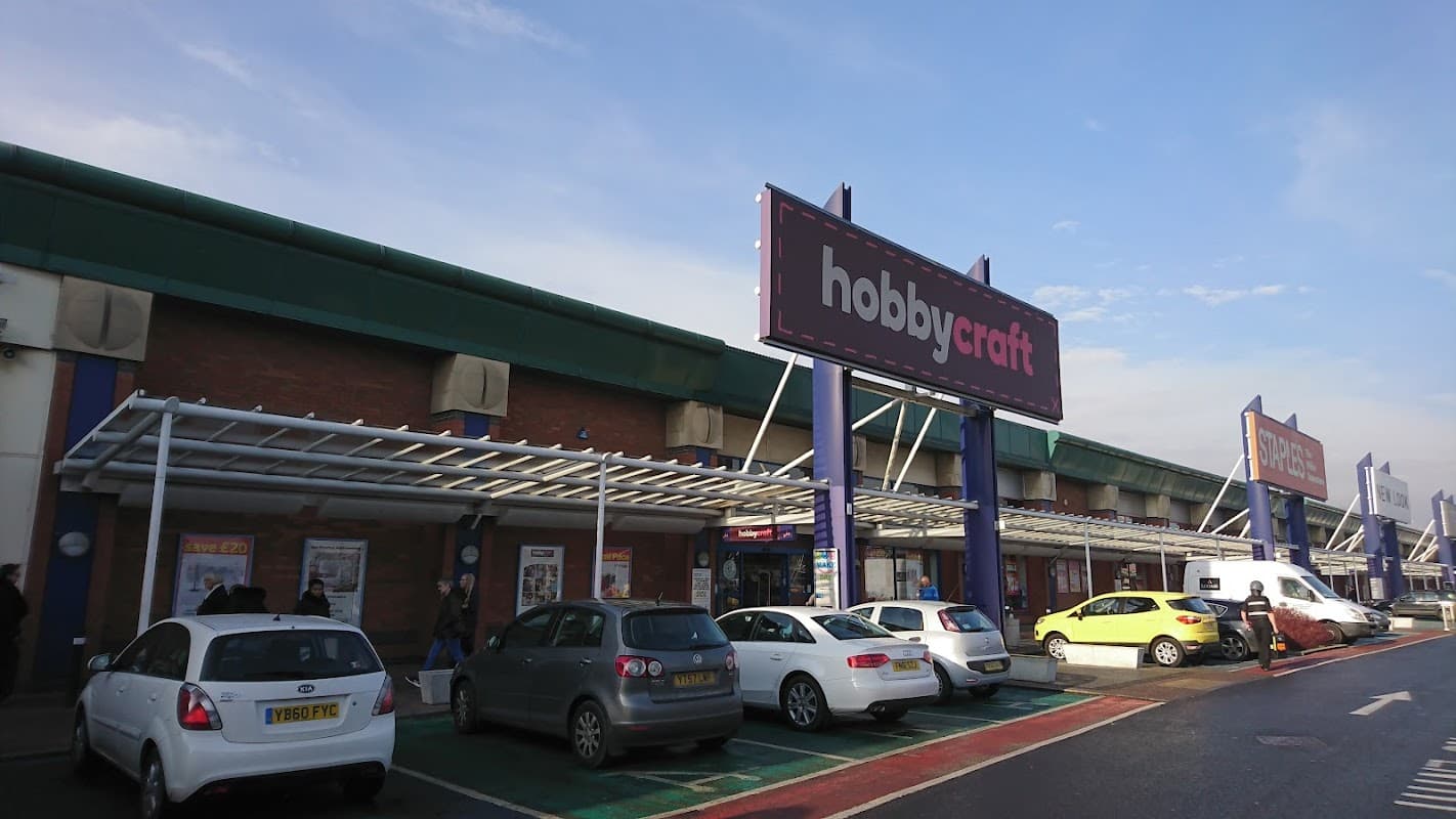 Hobbycraft storefront at Crown Point Shopping Park, with parked cars and clear blue sky in the background.