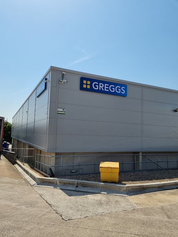 Greggs bakery building with a blue sign, clear sky, and a yellow bin nearby in Leeds, Yorkshire.