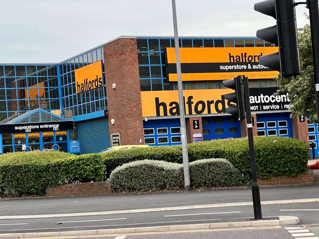 Halfords store with blue doors and windows, orange signage, and a green hedge in front, located on Meadow Lane, Leeds.