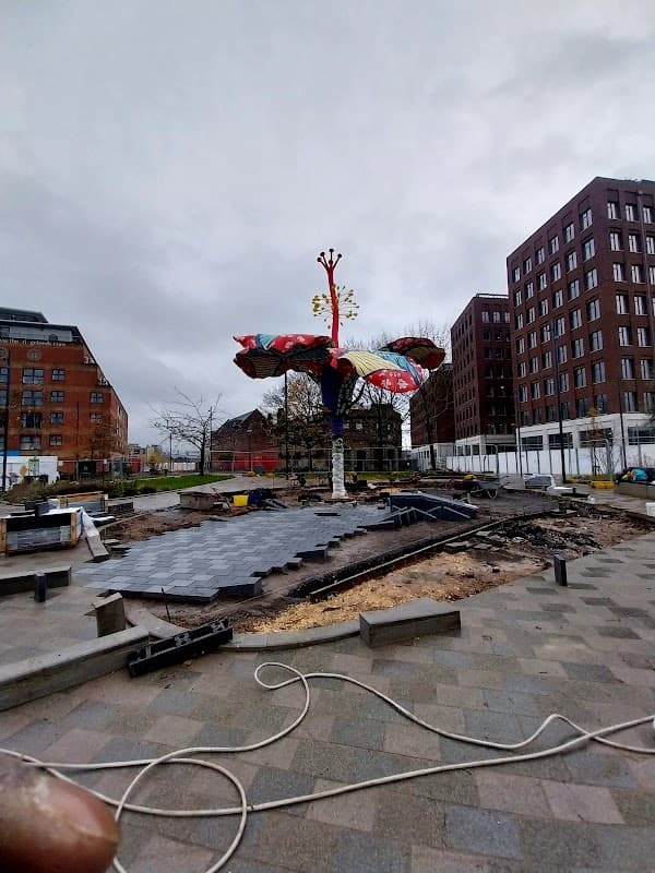 Colorful tree sculpture surrounded by construction materials and buildings in Leeds, Yorkshire under a cloudy sky.