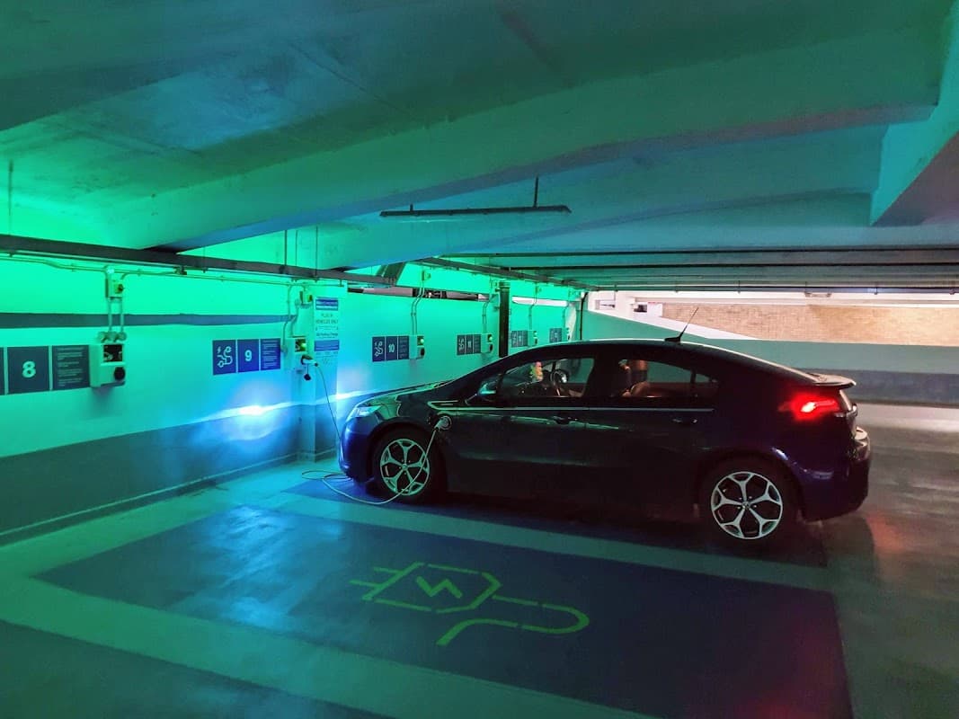Multi-storey car park featuring a parked car under green lighting, with numbered parking spaces visible on the walls.