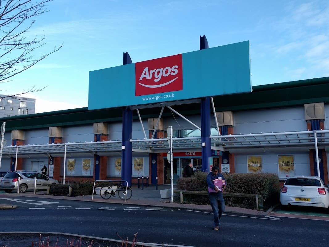 Argos store entrance with large sign, shoppers, and parked cars outside in Leeds, Yorkshire.