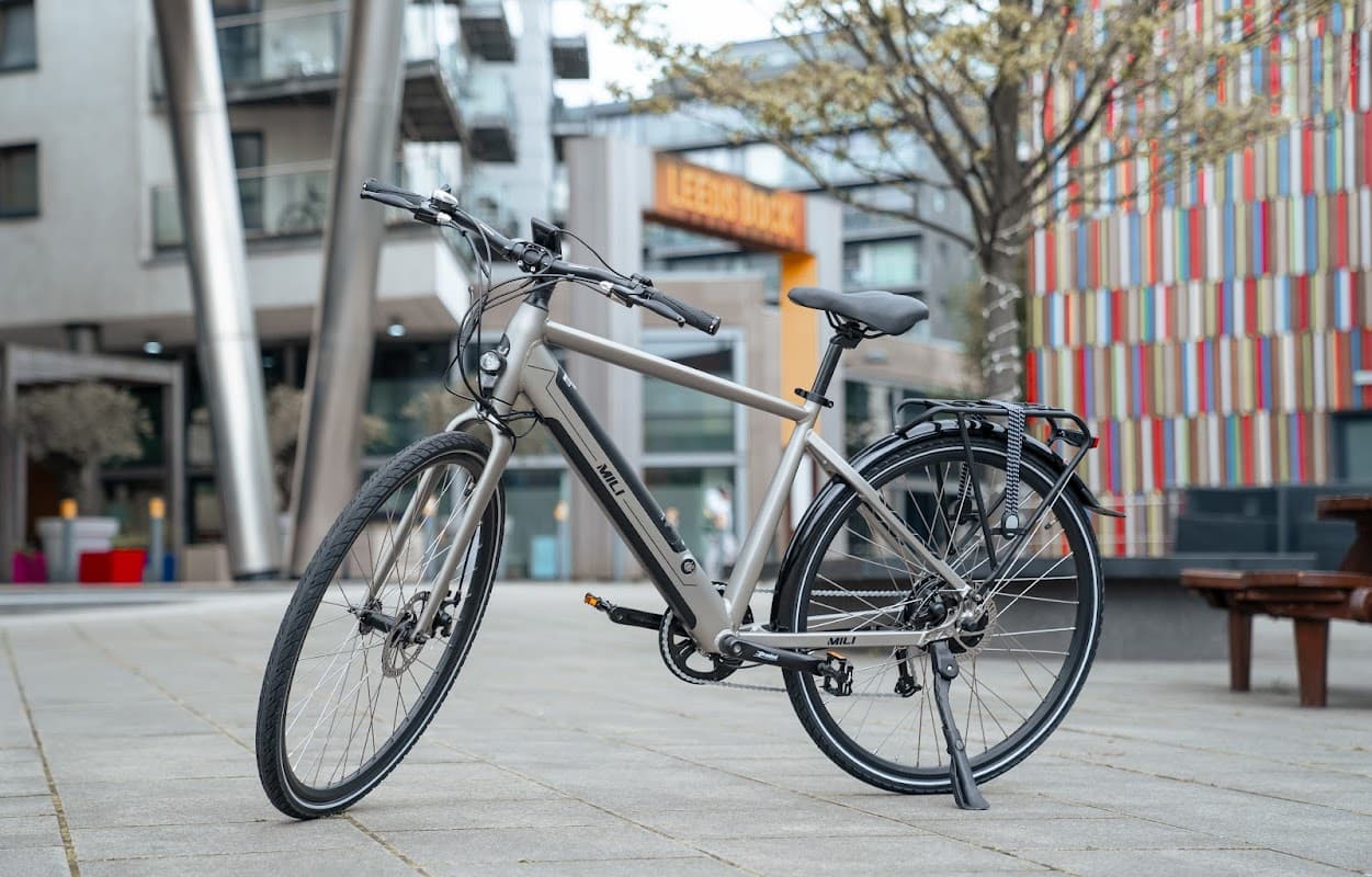 A sleek gray bike parked on a paved area with modern buildings and colorful facades in the background.