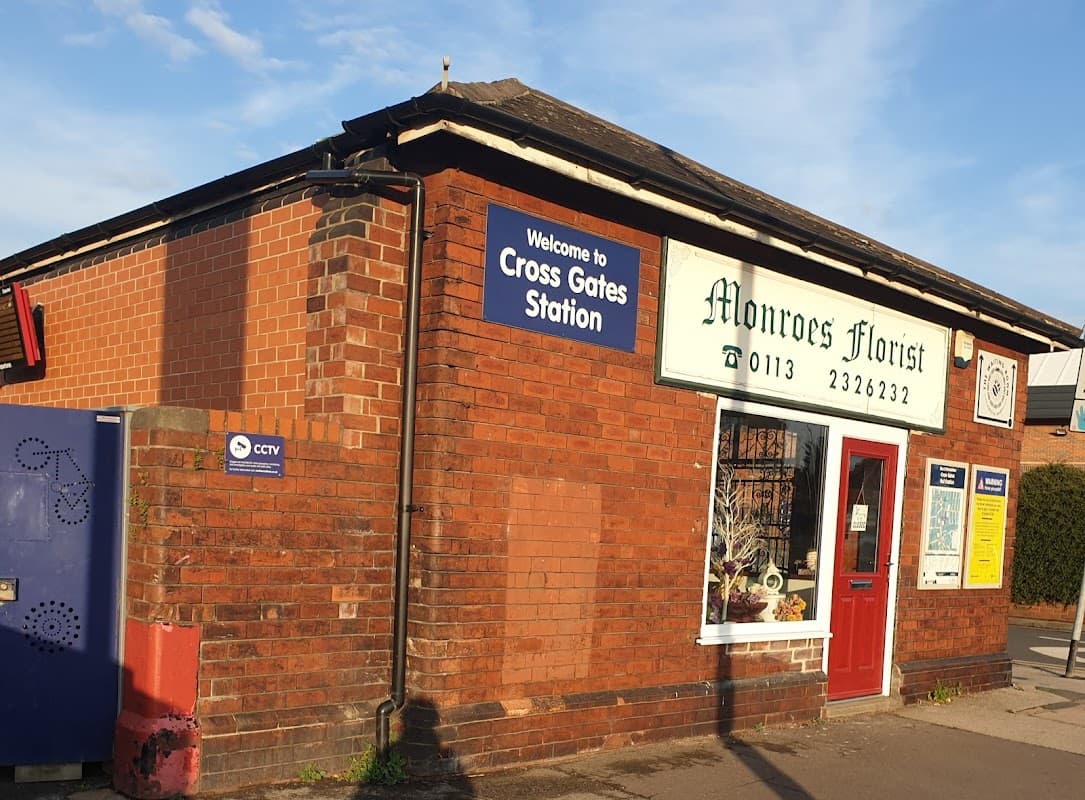 Brick building with a sign reading "Monroes Florist" and a nearby "Welcome to Cross Gates Station" sign.
