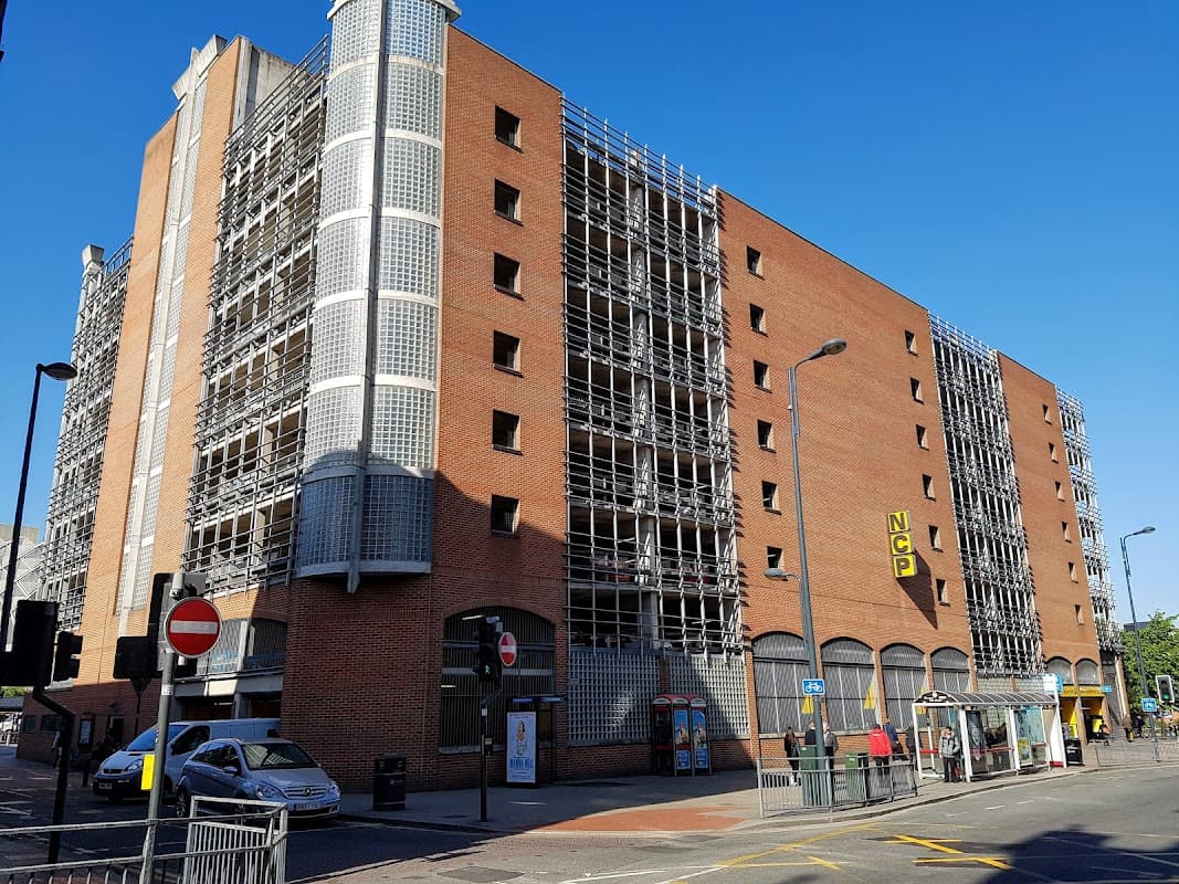 NCP Leeds The Markets car park with brick facade, scaffolding, and clear blue sky. Buses and cars in foreground.