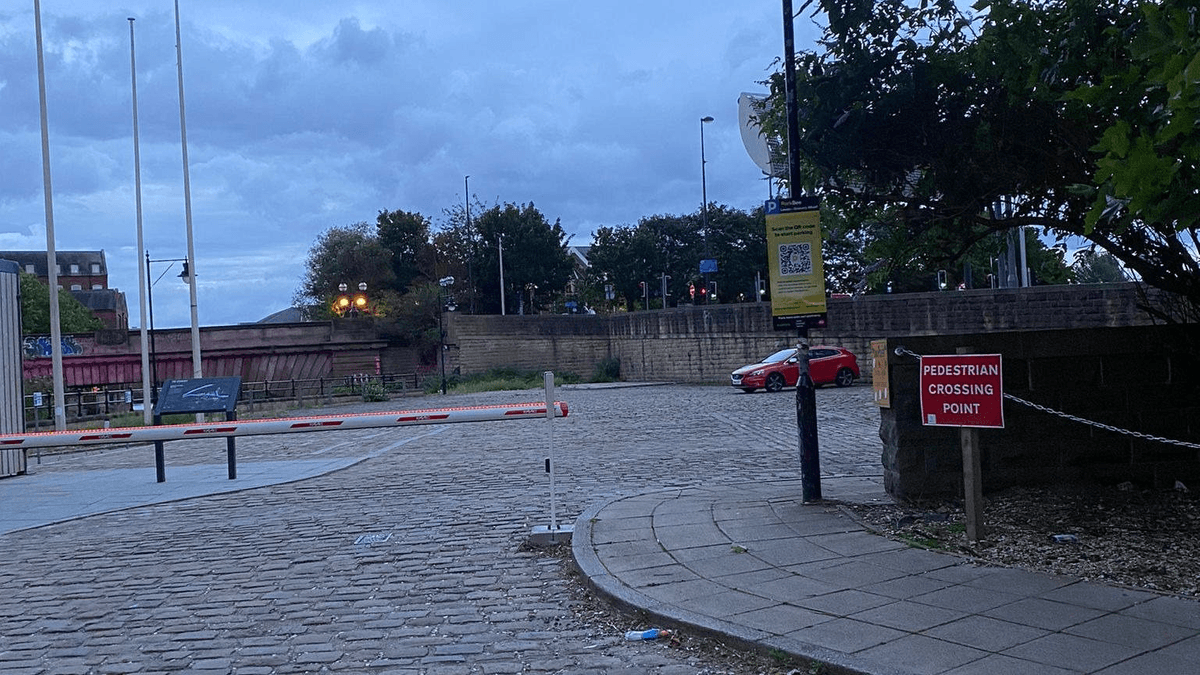 Cobblestone parking area at Granary Wharf, with a red car and a sign for pedestrian crossing point.