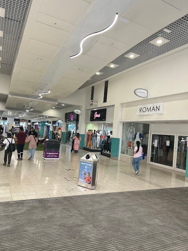 Interior view of St Johns Centre, featuring shops, shoppers, and a modern ceiling design with overhead lighting.