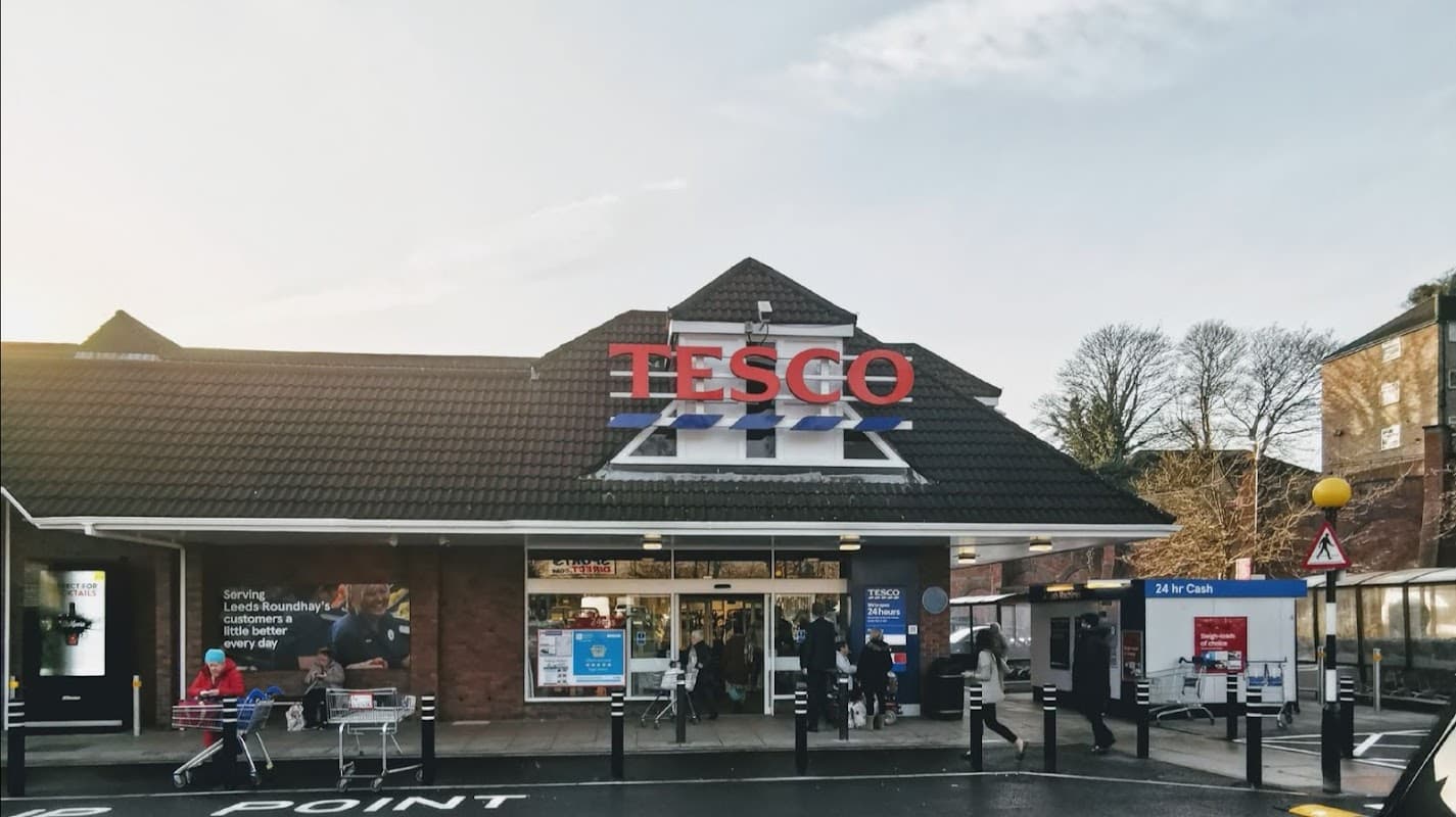 Tesco Superstore entrance with shoppers, bright signage, and parking area in Leeds, Yorkshire.