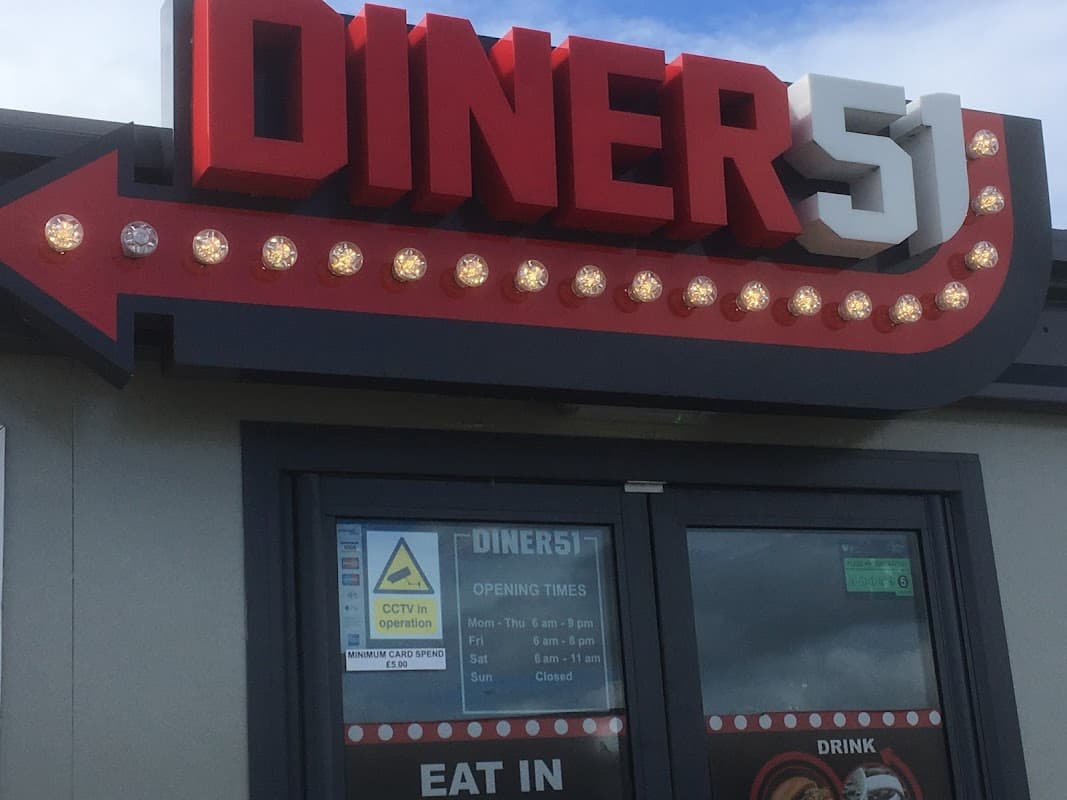 Brightly lit sign reading "DINER 51" with retro-style lights, featuring a window displaying opening times and a "CCTV in operation" notice.