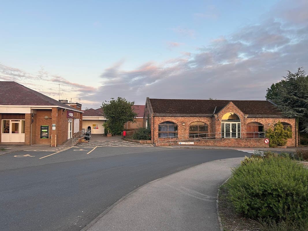 Moto Leeming Bar shop with brick facade, adjacent buildings, parking area, and trees under a colorful sky.