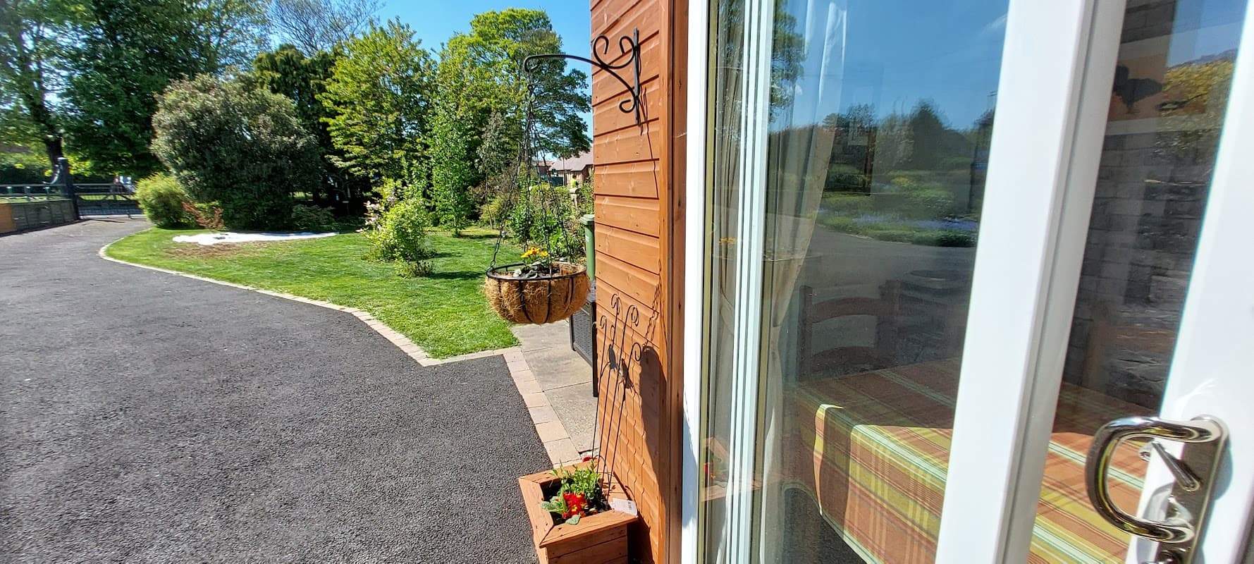 Bright exterior of The Roost Retreat with lush greenery, a flower basket, and a welcoming pathway in Leeming Bar, Yorkshire.