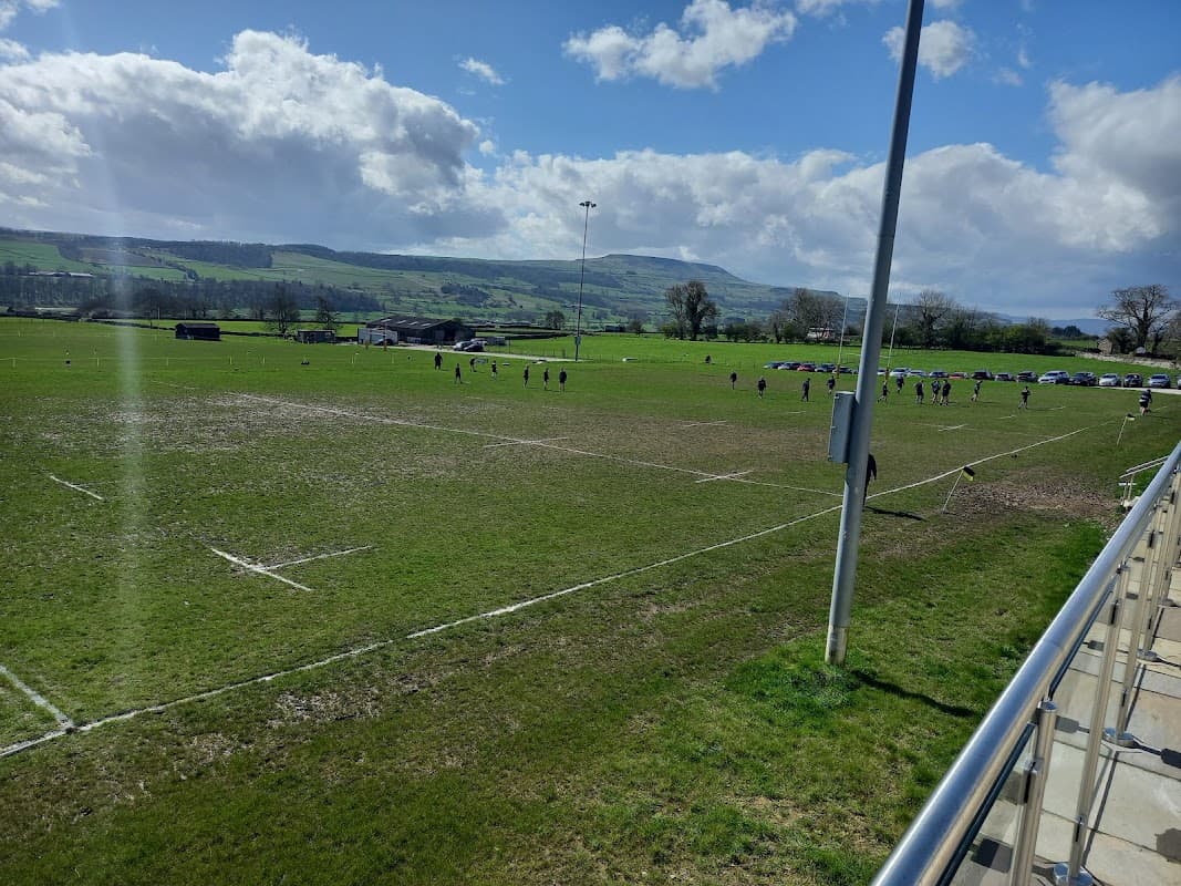 A rugby field with players in action, surrounded by hills and a clear blue sky in Leyburn, Yorkshire.