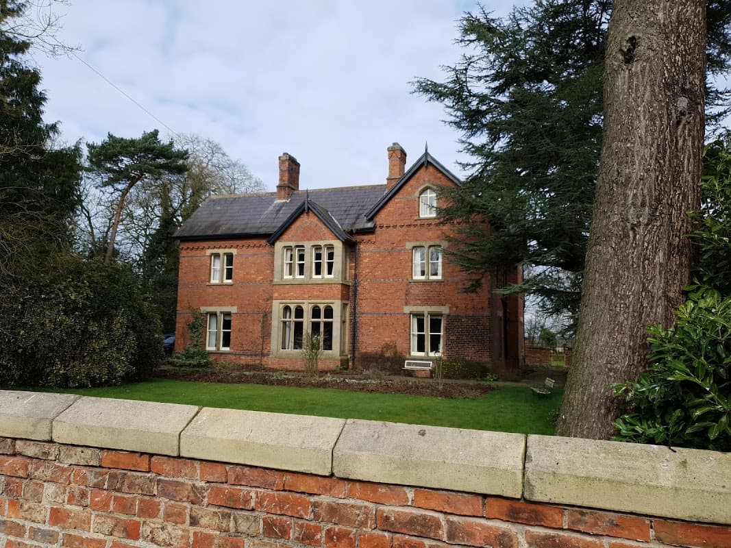 Victorian-style brick building with large windows, surrounded by greenery and a stone wall in Little Ouseburn.