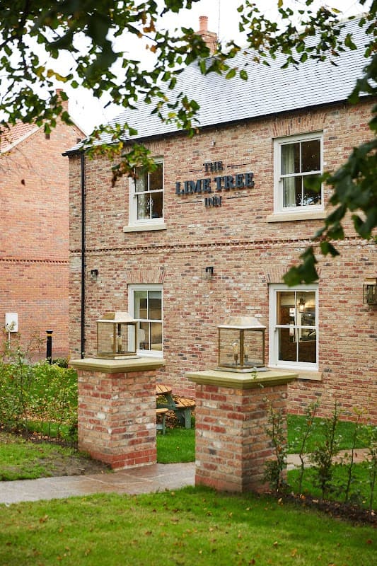 Brick building with "The Lime Tree Inn" sign, surrounded by greenery and a pathway leading to the entrance.