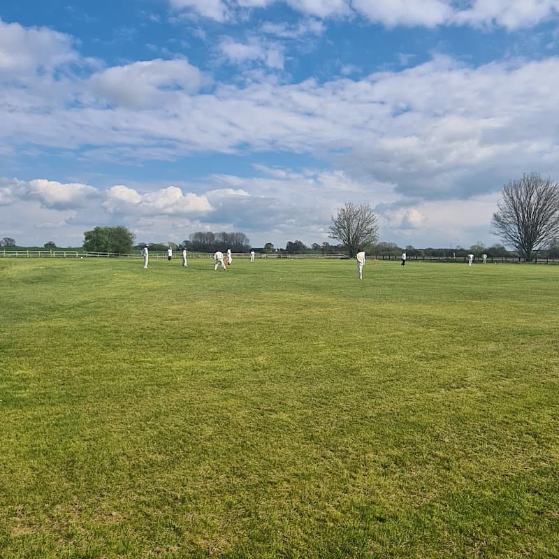 Cricket players in white uniforms on a green field under a blue sky with scattered clouds in Little Ribston, Yorkshire.