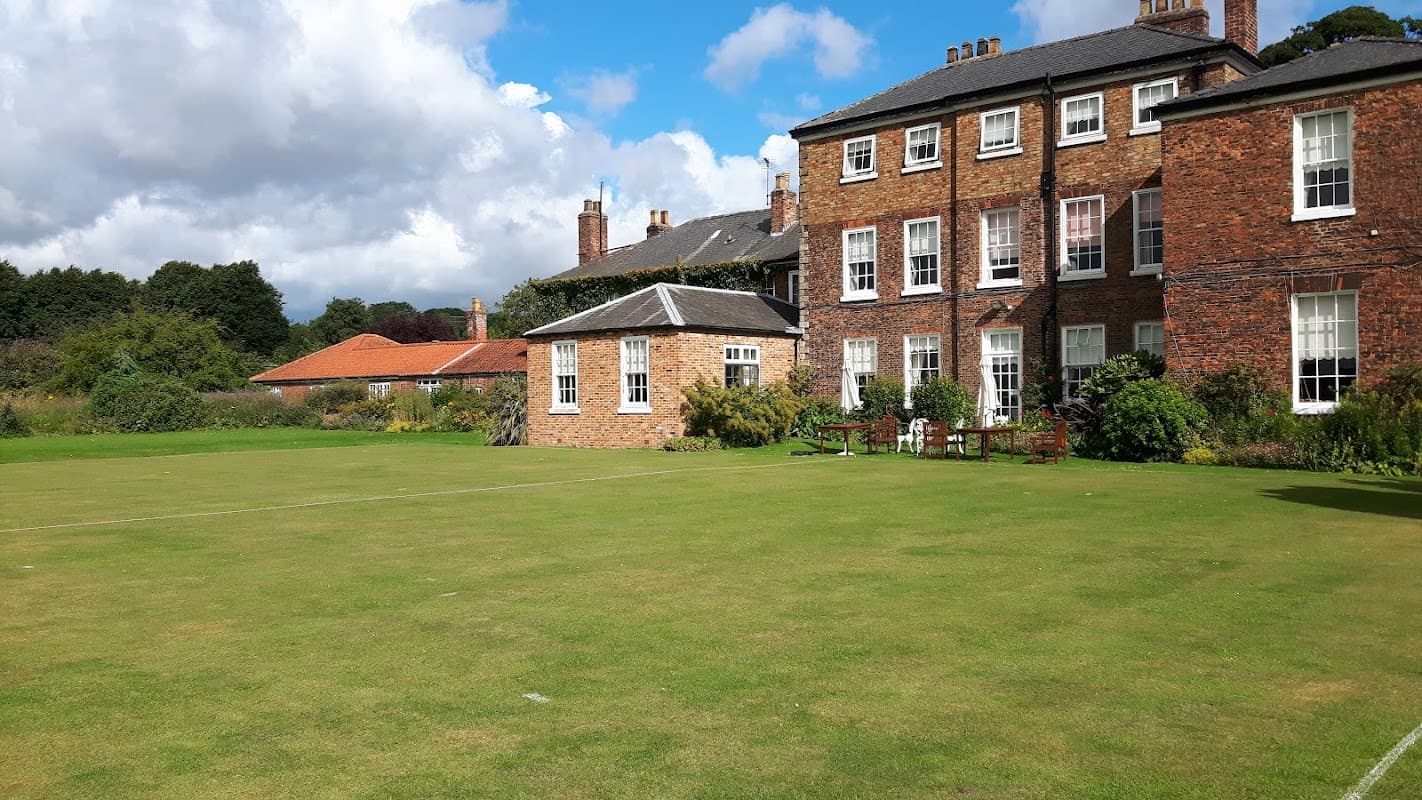 Historic brick building with large windows, manicured lawn, and blue sky with clouds in Little Weighton, Yorkshire.