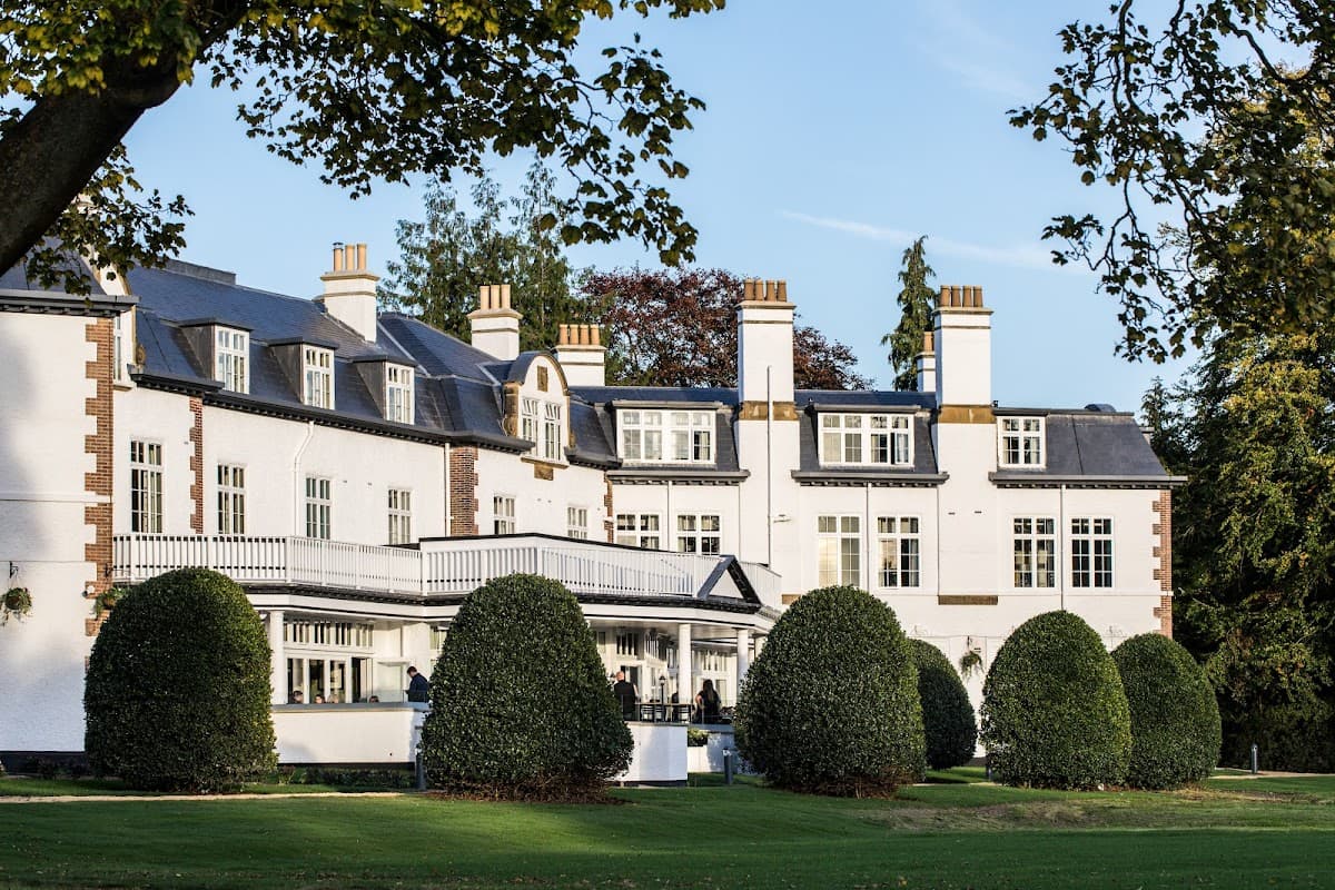 The Ripon Inn features a white facade, multiple chimneys, and manicured hedges in a lush green setting.