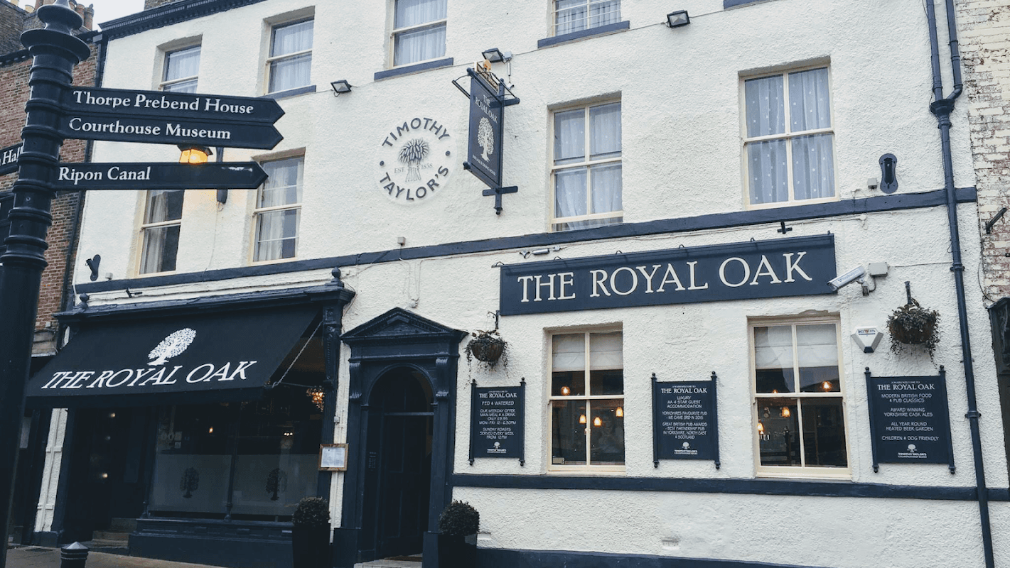 The Royal Oak pub featuring a black awning, large windows, and a sign with the pub's name in white lettering.