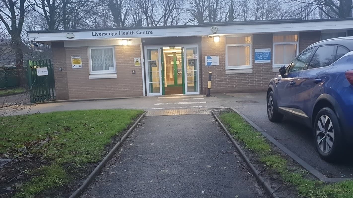 Liversedge Health Centre entrance with a blue car parked nearby, surrounded by grass and trees.