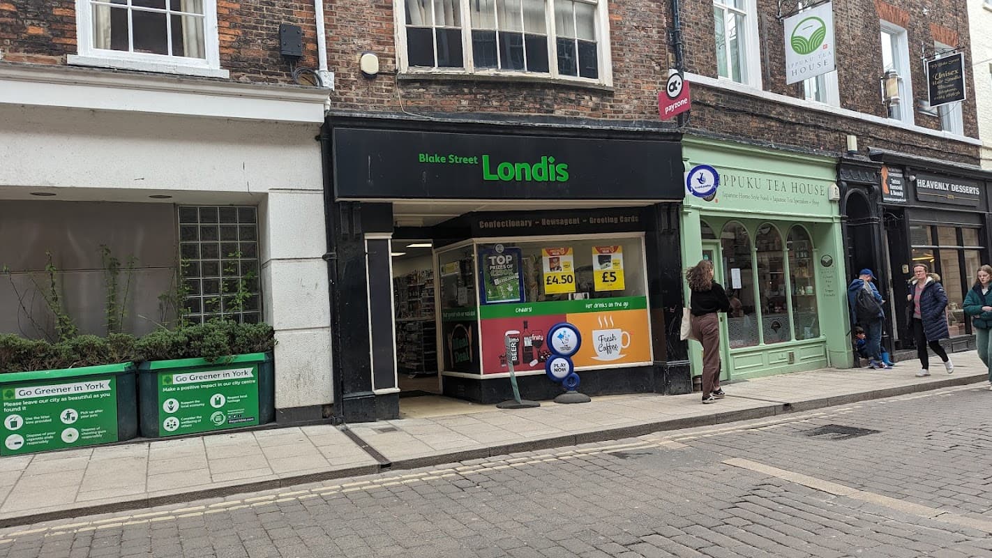 Londis grocery store entrance with signage, shoppers outside, and nearby green tea house in Liversedge, Yorkshire.