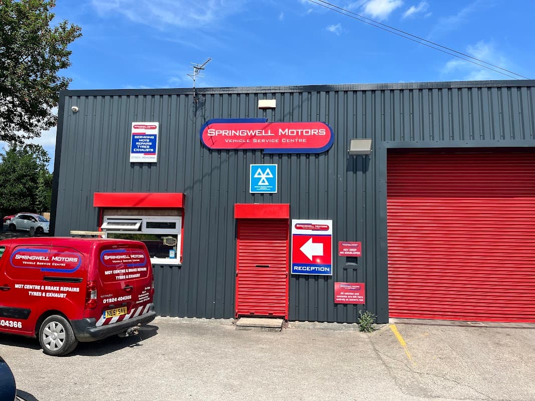 Springwell Motors building with red signage, a reception area, and a service van parked outside under a clear blue sky.