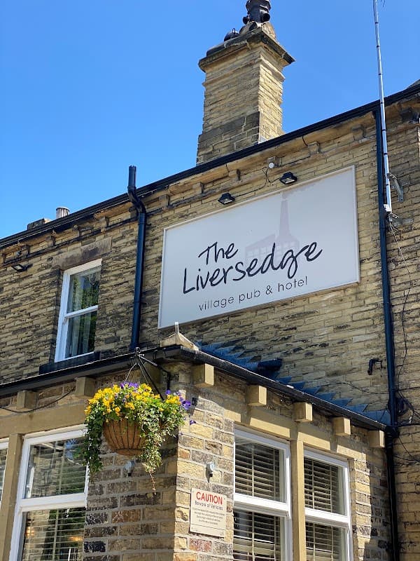 Sign for "The Liversedge" pub and hotel on a stone building, with a hanging flower basket and clear blue sky.
