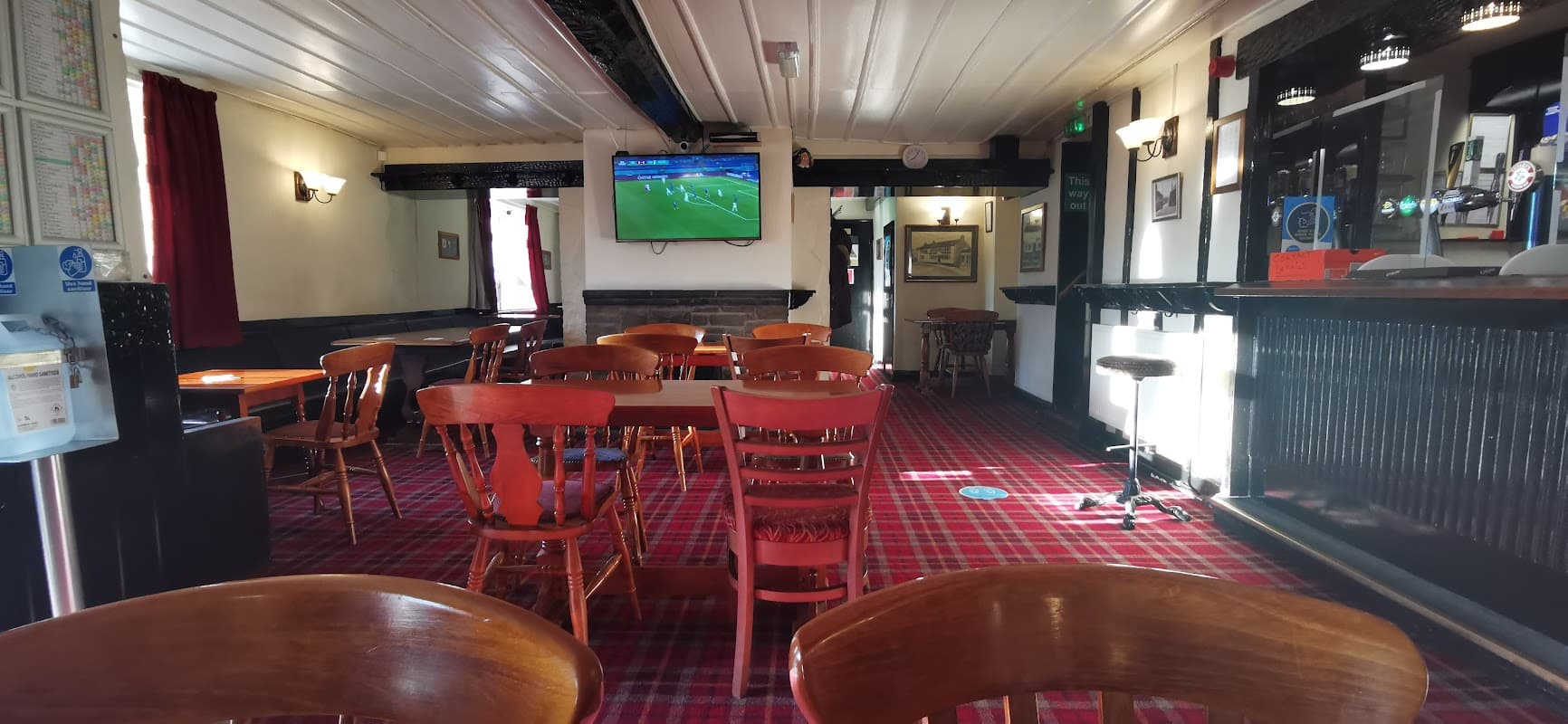 Interior of The Toby Jug bar featuring wooden tables, chairs, a bar counter, and a TV showing a sports event.